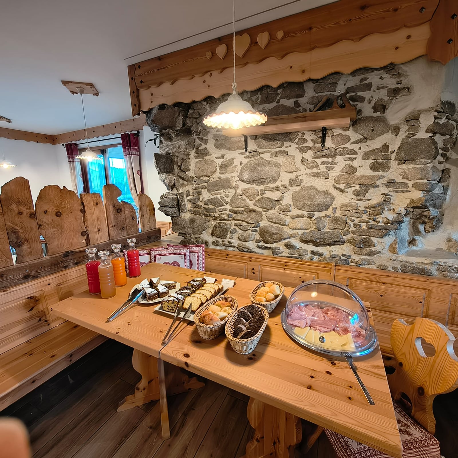Buffet della colazione con dolci, pane, salumi e formaggi nella sala in legno e pietra