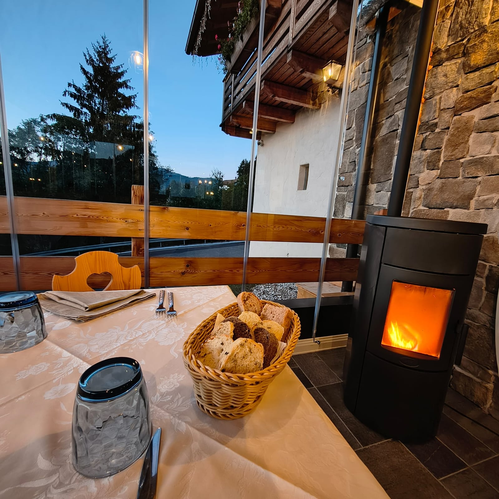 Cestino di pane sulla tavola della terrazza vetrata, accanto alla stufa accesa e con vista serale sulle montagne